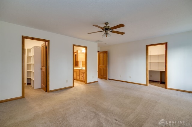 unfurnished bedroom featuring connected bathroom, a walk in closet, light carpet, a closet, and ceiling fan