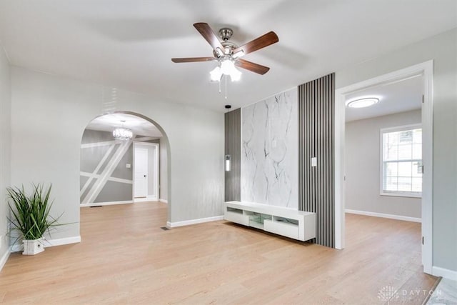 unfurnished room featuring arched walkways, wood finished floors, a ceiling fan, and baseboards