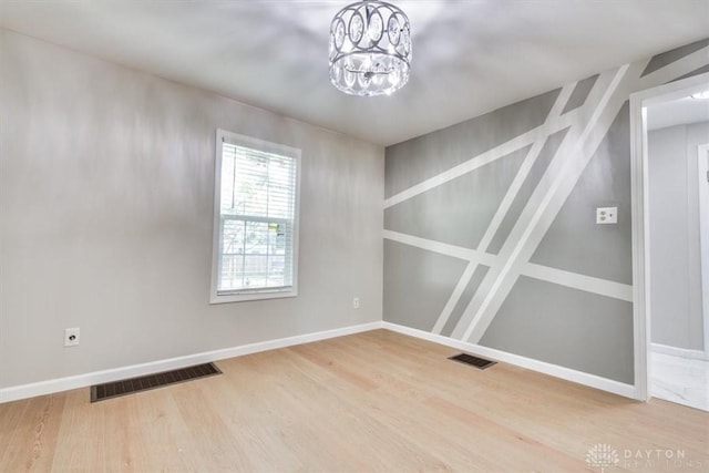 empty room with an inviting chandelier, baseboards, visible vents, and wood finished floors