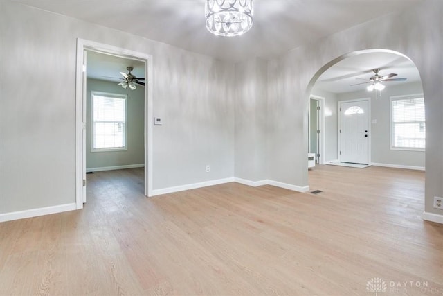 entrance foyer with light wood-style flooring, arched walkways, baseboards, and ceiling fan with notable chandelier