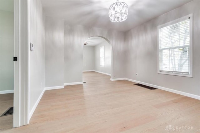 empty room featuring arched walkways, light wood-style flooring, visible vents, and baseboards