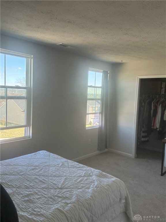 carpeted bedroom featuring a textured ceiling, multiple windows, and a closet