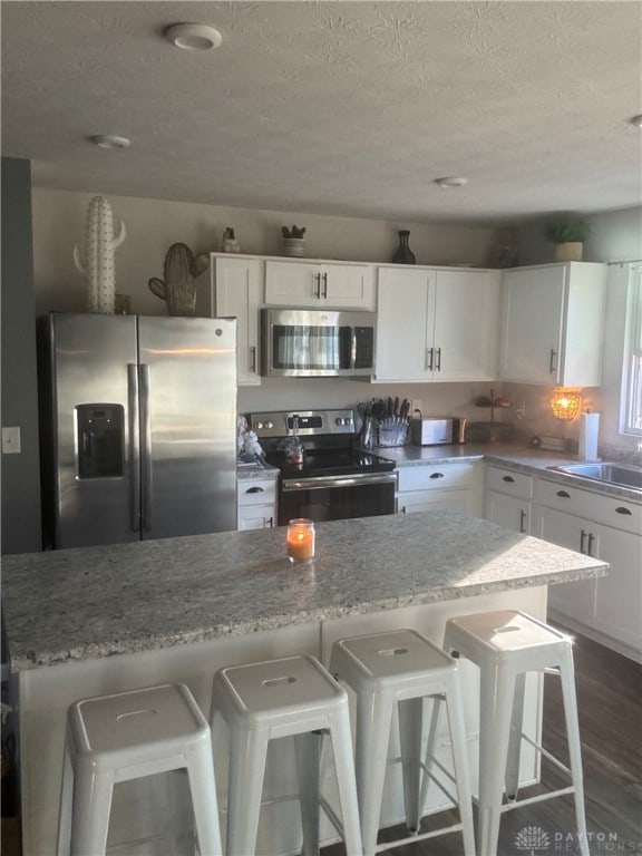 kitchen with a kitchen bar, appliances with stainless steel finishes, a textured ceiling, and white cabinets