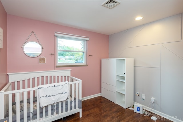 bedroom with dark hardwood / wood-style floors and a nursery area