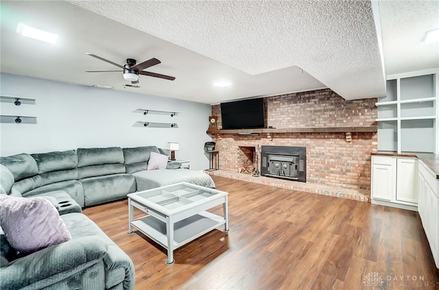 living room featuring a wood stove, brick wall, a textured ceiling, light hardwood / wood-style floors, and ceiling fan