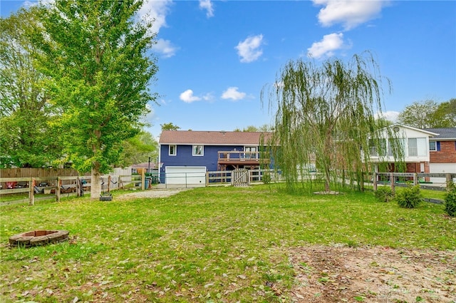 back of house featuring a garage, a deck, a lawn, and an outdoor fire pit