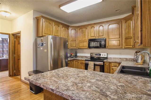 kitchen featuring sink, a textured ceiling, kitchen peninsula, light hardwood / wood-style flooring, and appliances with stainless steel finishes