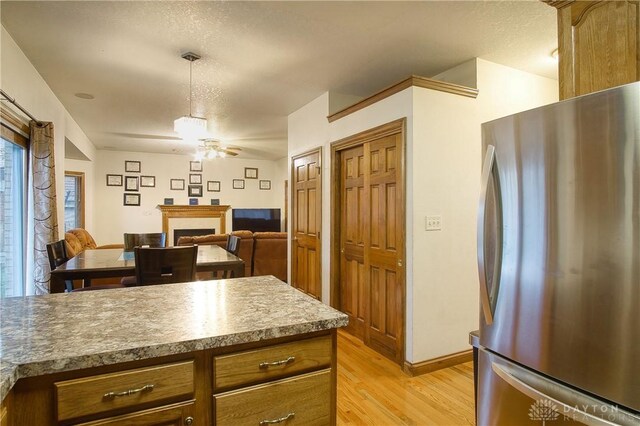 kitchen with a textured ceiling, ceiling fan, light hardwood / wood-style floors, hanging light fixtures, and stainless steel fridge