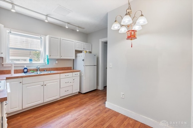 kitchen with white cabinets, track lighting, pendant lighting, sink, and white refrigerator