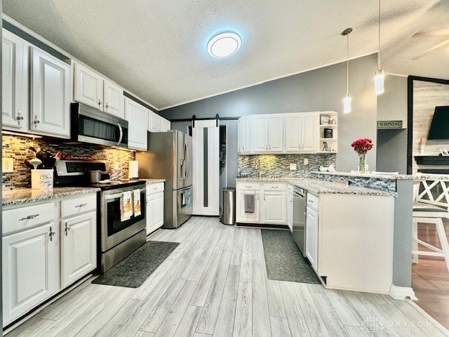 kitchen featuring white cabinets, stainless steel appliances, vaulted ceiling, and hanging light fixtures