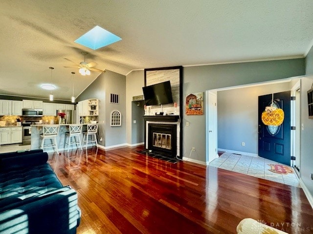 living room featuring a textured ceiling, hardwood / wood-style floors, ceiling fan, vaulted ceiling with skylight, and ornamental molding