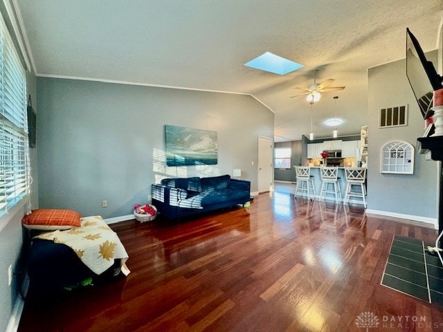 living room with ceiling fan, crown molding, vaulted ceiling with skylight, and dark hardwood / wood-style floors