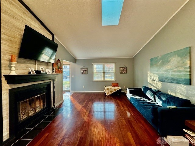 living room with ornamental molding, dark hardwood / wood-style floors, a tiled fireplace, and vaulted ceiling