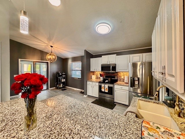 kitchen featuring lofted ceiling, white cabinetry, stainless steel appliances, and hanging light fixtures