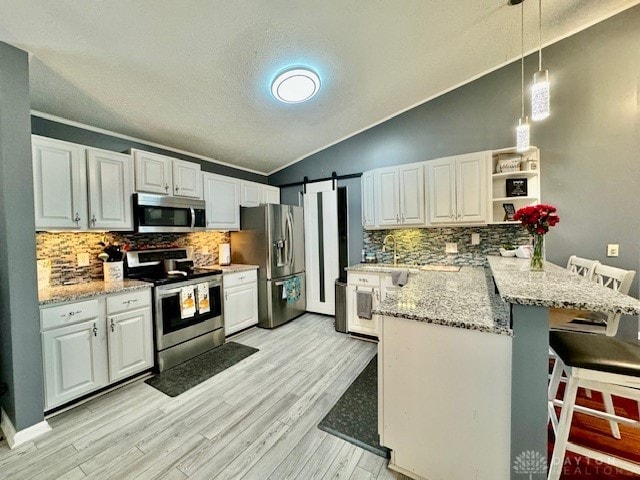 kitchen with appliances with stainless steel finishes, a kitchen bar, a barn door, kitchen peninsula, and white cabinets