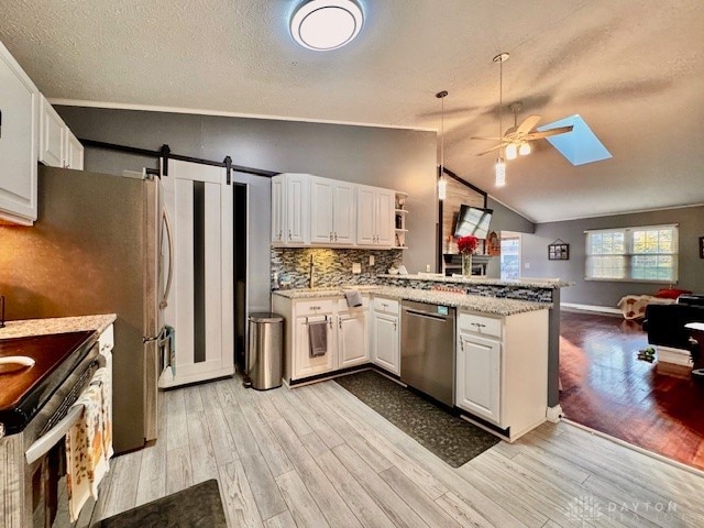 kitchen with vaulted ceiling with skylight, stainless steel appliances, white cabinetry, and light hardwood / wood-style floors