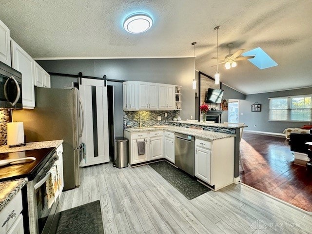 kitchen featuring kitchen peninsula, stainless steel appliances, vaulted ceiling with skylight, light wood-type flooring, and white cabinetry