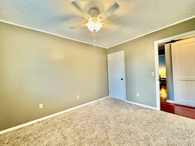 unfurnished bedroom with a textured ceiling, a barn door, carpet flooring, and ceiling fan