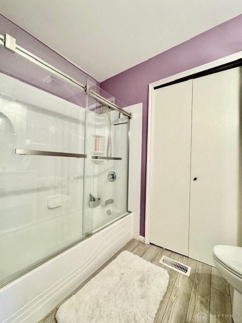 bathroom with hardwood / wood-style floors, bath / shower combo with glass door, and toilet