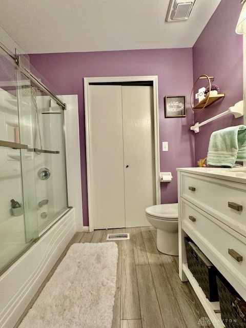 full bathroom featuring vanity, hardwood / wood-style floors, bath / shower combo with glass door, and toilet