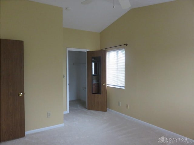 unfurnished bedroom featuring lofted ceiling, baseboards, a walk in closet, and light colored carpet