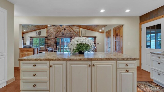 kitchen featuring light stone countertops, a kitchen island, vaulted ceiling, and light wood-type flooring