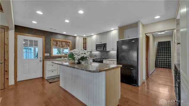 kitchen featuring black appliances, white cabinets, a kitchen island, and light hardwood / wood-style floors