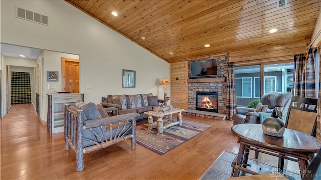 living room with light hardwood / wood-style floors, a stone fireplace, high vaulted ceiling, and wood ceiling