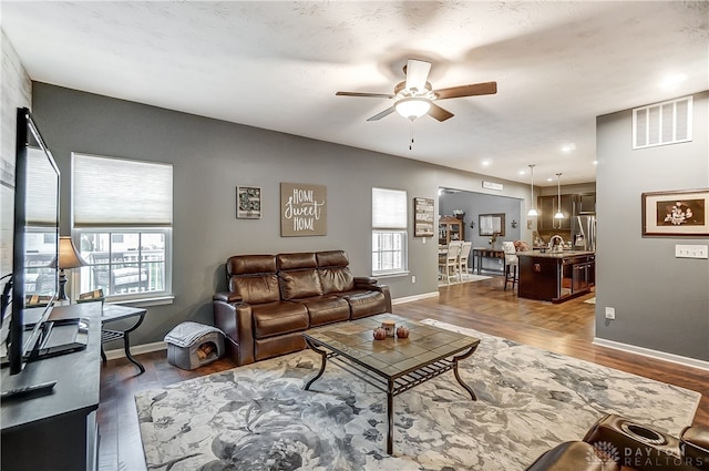 living room featuring plenty of natural light, ceiling fan, sink, and dark wood-type flooring