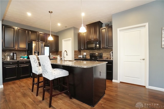 kitchen with a kitchen island with sink, black appliances, sink, decorative light fixtures, and dark hardwood / wood-style flooring