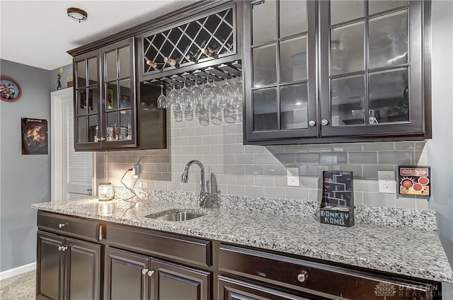 bar with light stone countertops, dark brown cabinetry, tasteful backsplash, and sink