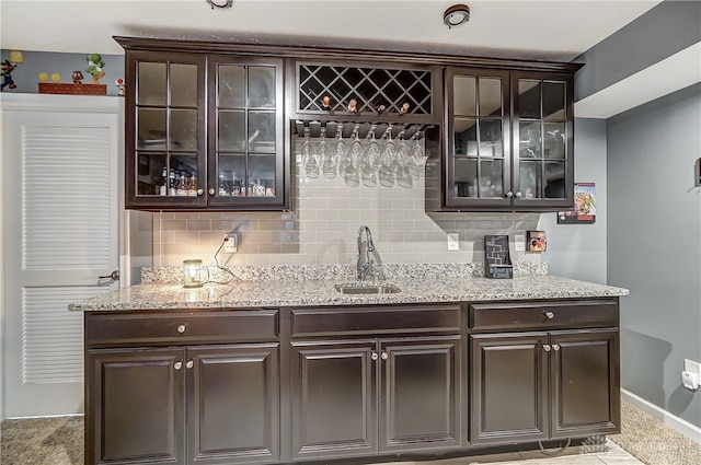 bar with dark brown cabinetry, decorative backsplash, sink, and light stone countertops