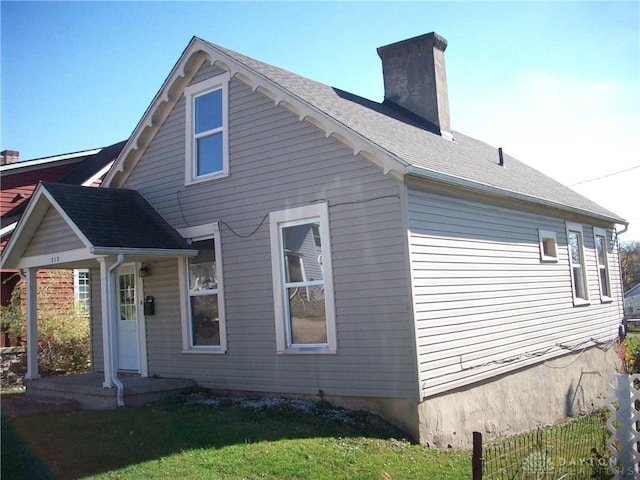 back of property featuring a shingled roof, a chimney, and a lawn