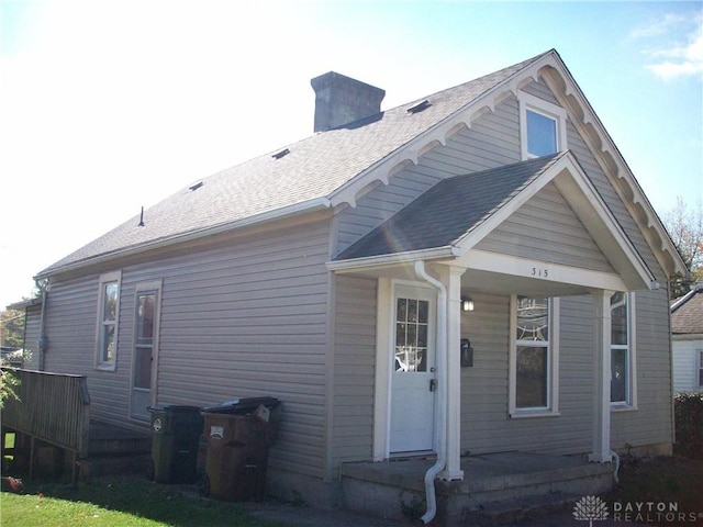 back of house featuring roof with shingles and a chimney