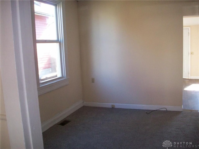 empty room featuring baseboards, visible vents, and dark carpet