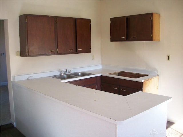 kitchen with a peninsula, black electric cooktop, dark brown cabinets, light countertops, and a sink