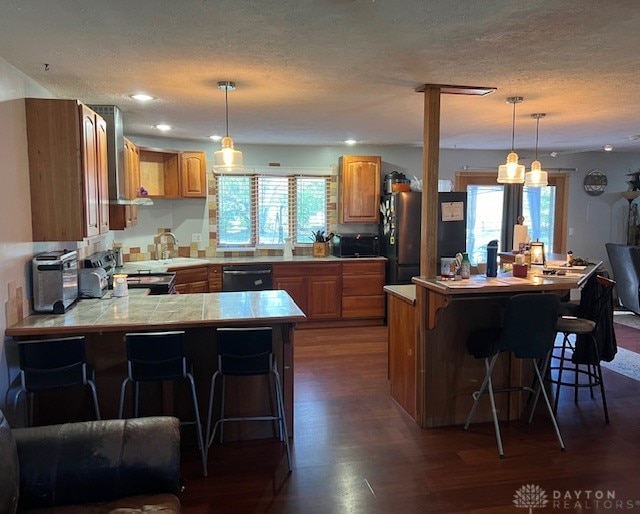 kitchen with a breakfast bar, appliances with stainless steel finishes, dark hardwood / wood-style floors, and pendant lighting