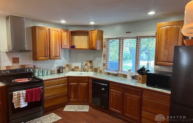 kitchen featuring dark wood-type flooring, sink, black appliances, and wall chimney range hood