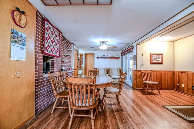 dining room featuring brick wall, hardwood / wood-style floors, a large fireplace, and ceiling fan