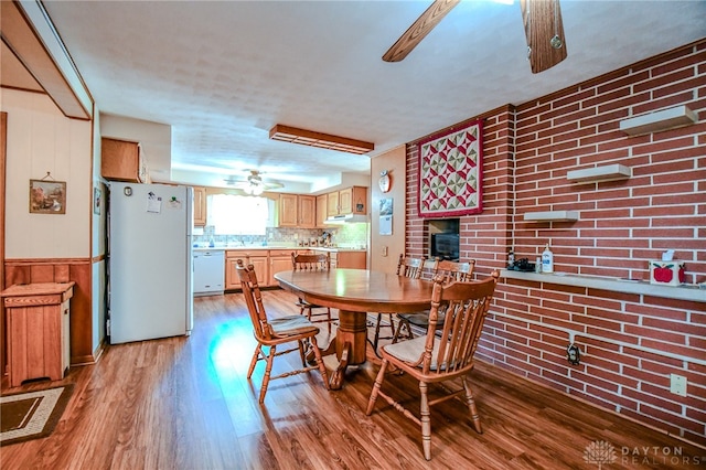 dining room featuring ceiling fan, brick wall, a fireplace, and hardwood / wood-style floors