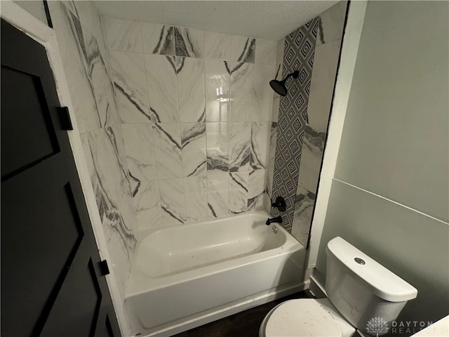 bathroom featuring toilet, tiled shower / bath combo, and a textured ceiling