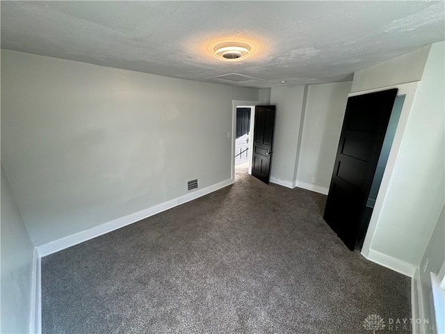 spare room featuring dark colored carpet and a textured ceiling