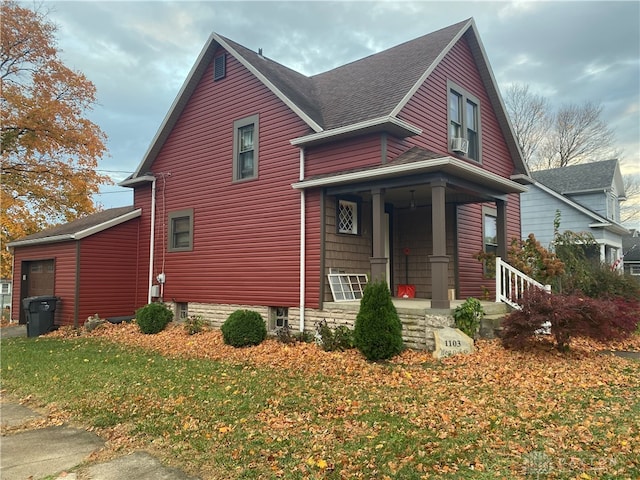 view of front of property featuring cooling unit, a garage, a porch, a front lawn, and an outbuilding