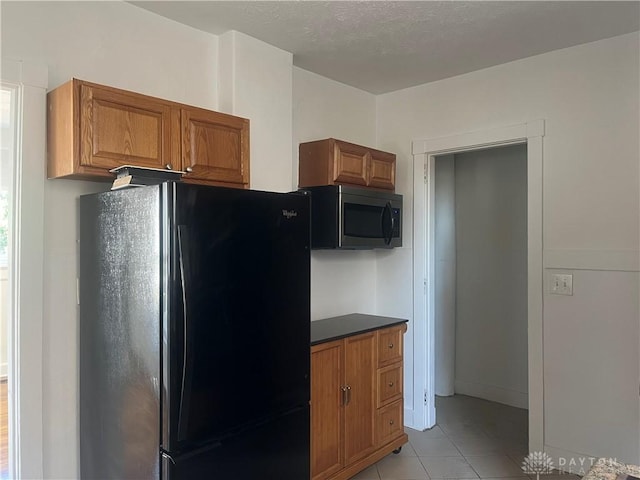 kitchen with light tile patterned flooring, black refrigerator, and a textured ceiling