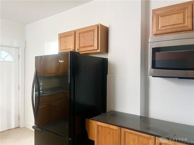 kitchen featuring black refrigerator, dark stone counters, and light tile patterned floors