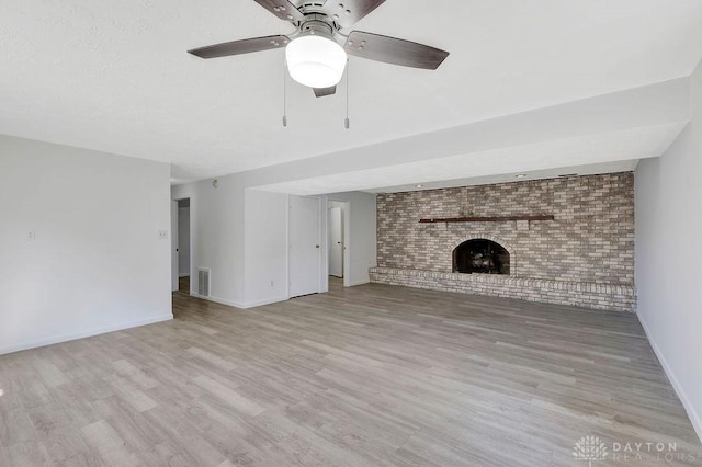 unfurnished living room featuring ceiling fan, light hardwood / wood-style floors, brick wall, and a brick fireplace