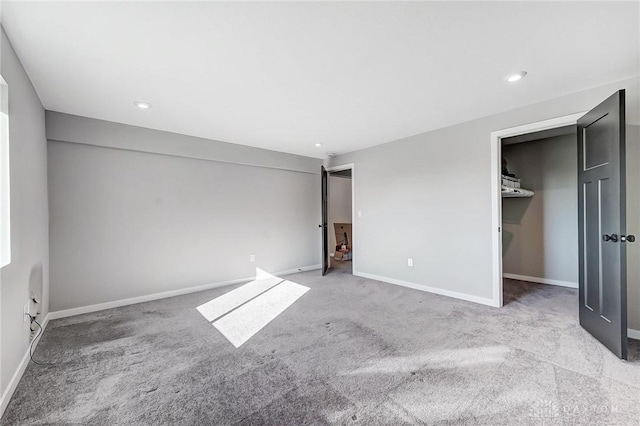 unfurnished bedroom featuring carpet floors, baseboards, a walk in closet, and recessed lighting