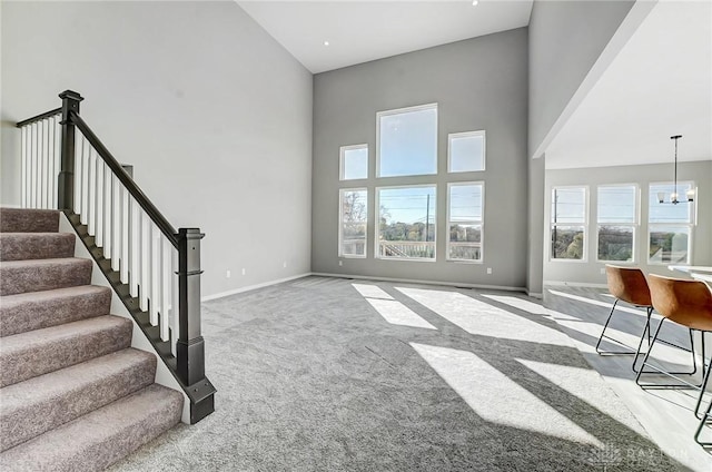 unfurnished living room featuring carpet flooring, healthy amount of natural light, a towering ceiling, baseboards, and stairway