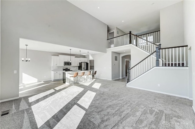 unfurnished living room with light carpet, a towering ceiling, stairway, baseboards, and a sink