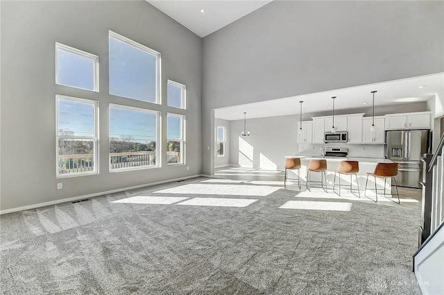 unfurnished living room featuring light carpet, a high ceiling, and baseboards